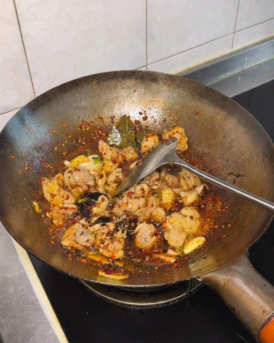 Salsa de soja y condimentos siendo incorporados al pollo salteado en el wok.