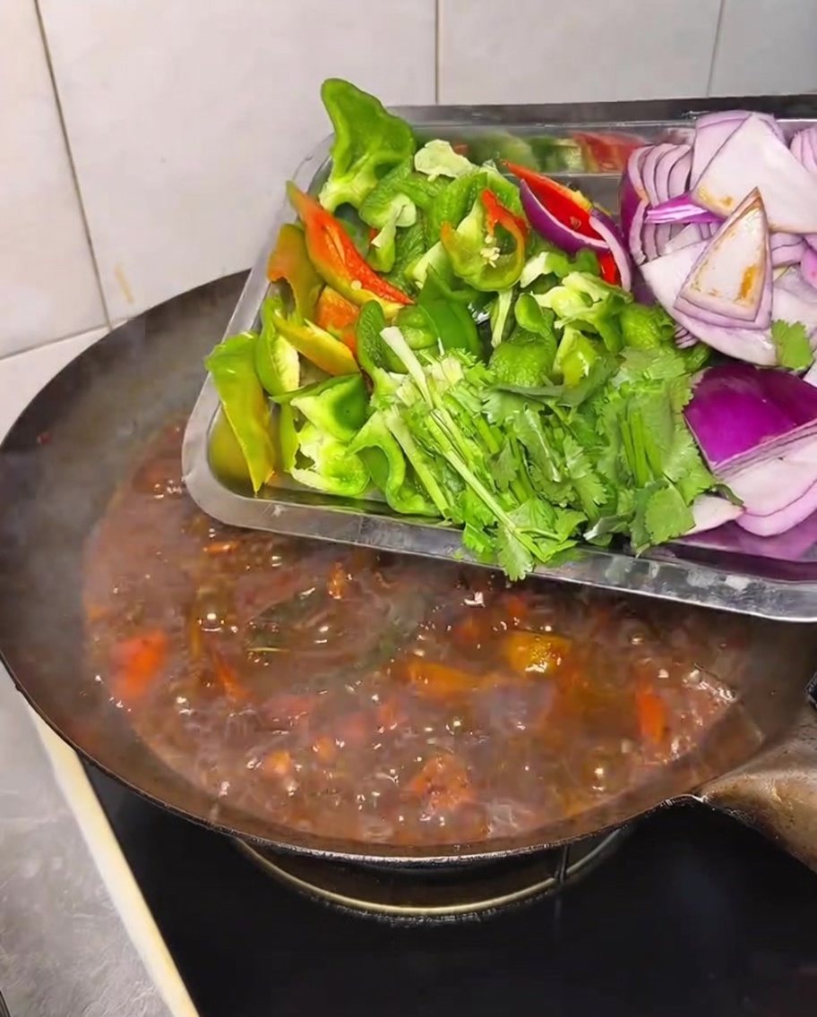 Pimientos frescos, cebolla y cilantro siendo añadidos a un wok de pollo y verduras.