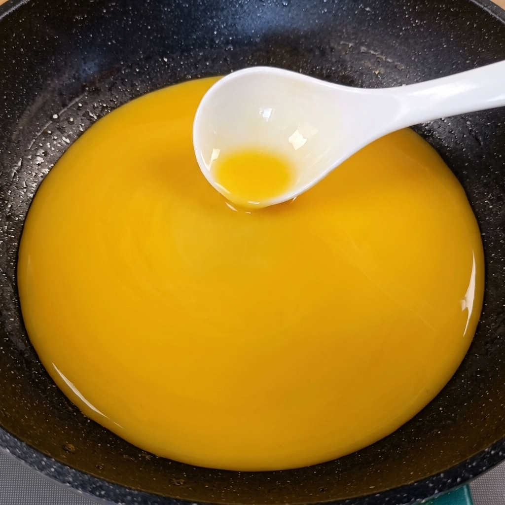 Una salsa espesa de color amarillo dorado siendo removida en una sartén oscura con un cucharón blanco.