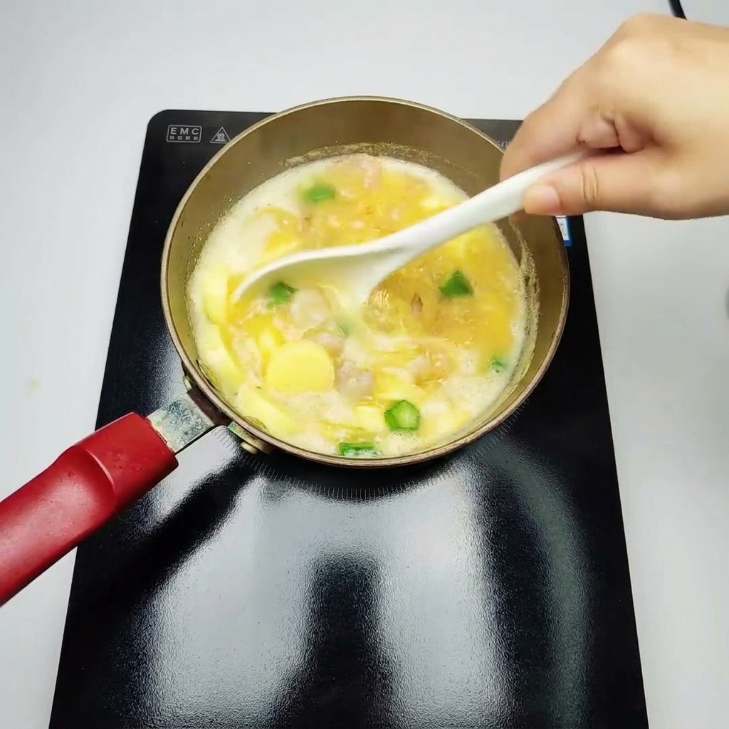 Un cucharón blanco revolviendo suavemente una sopa amarilla a fuego lento llena de camarones cocidos, trozos de quimbombó verde y tofu de huevo en rodajas.