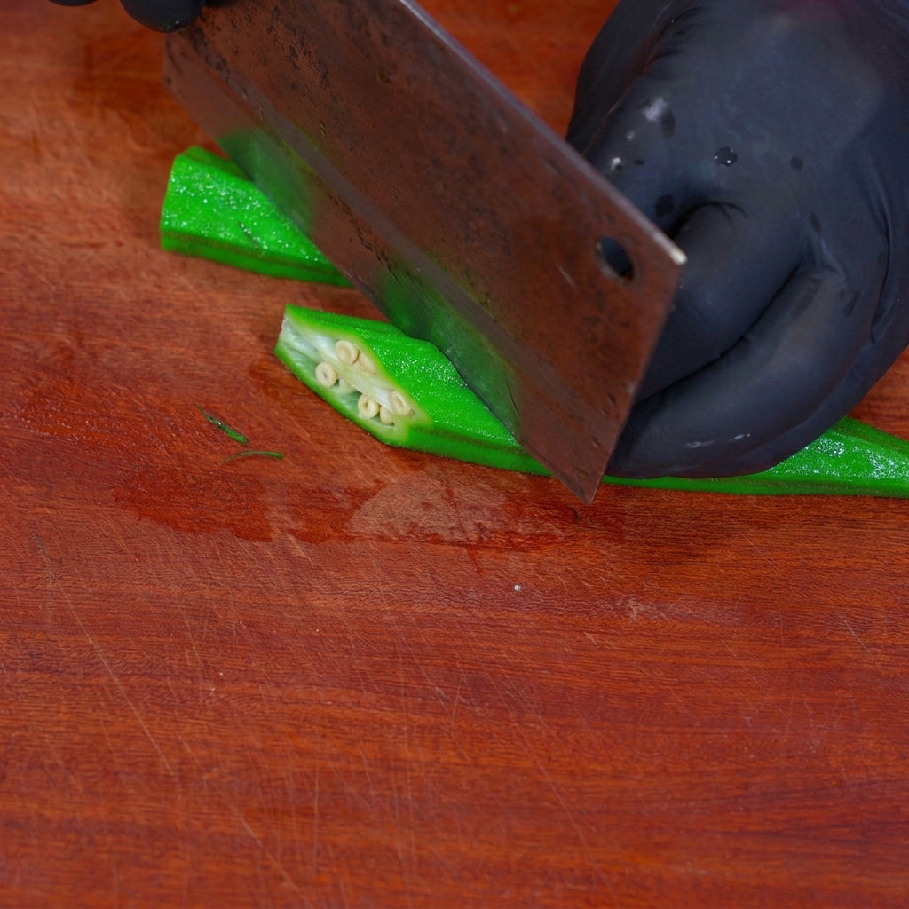 Okra blanqueada cortándose en piezas con forma de diamante sobre una tabla.