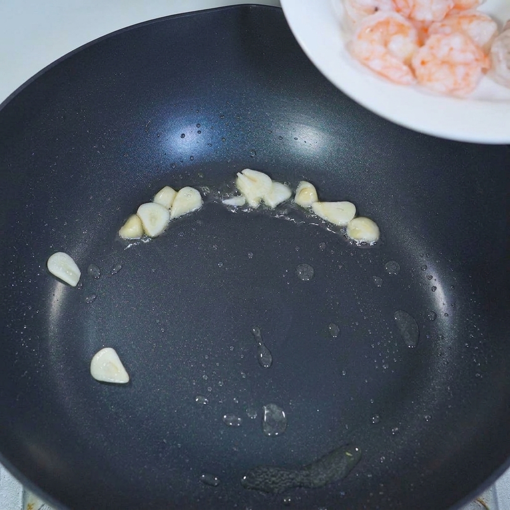 Gambas previamente cocinadas siendo añadidas a una sartén con ajo sofrito.