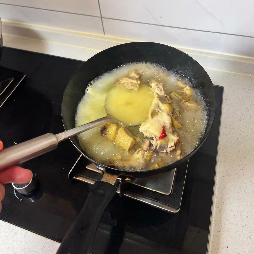 Un cucharón removiendo caldo de pollo caliente y trozos de pollo en un wok negro.