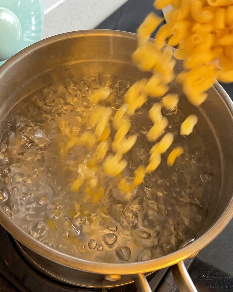 Pasta de macarrones seca siendo vertida en una olla con agua hirviendo.