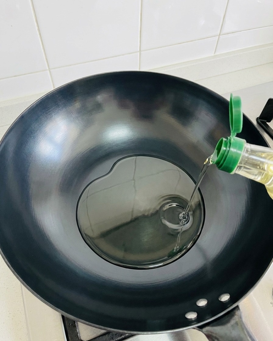 Aceite de oliva siendo vertido en un wok oscuro caliente y vacío.