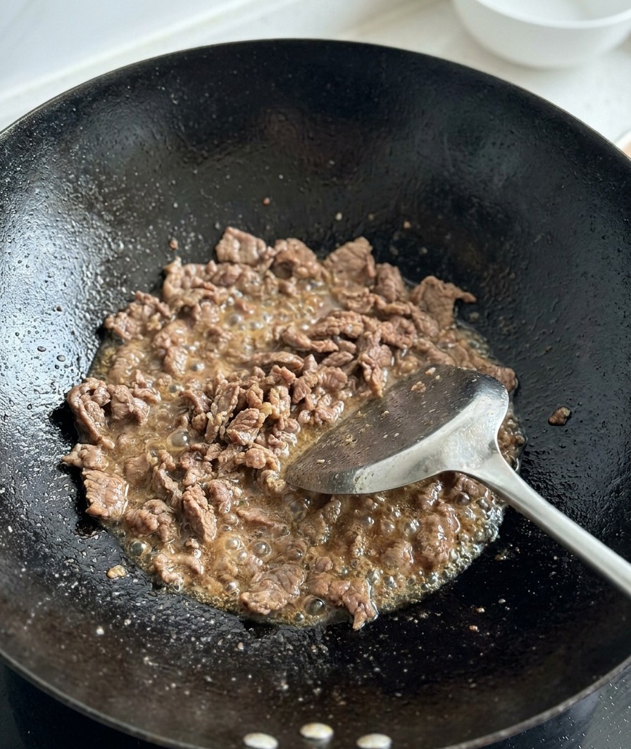 Tomates troceados frescos siendo añadidos a la carne dorada en un wok.