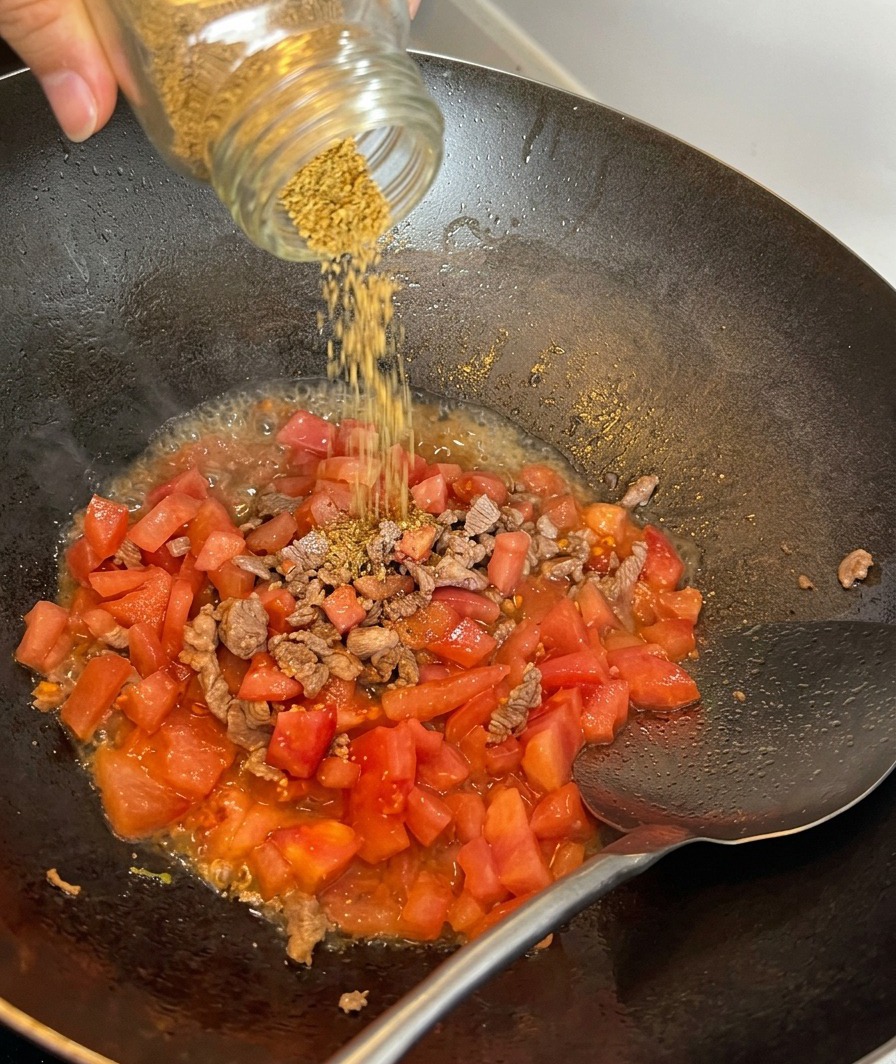 Sal marina siendo espolvoreada sobre una mezcla de ternera salteada y tomates troceados.