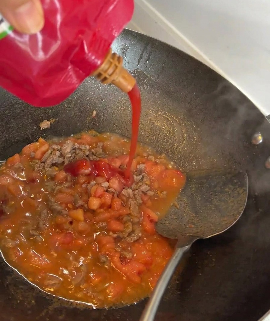 Concentrado de tomate siendo vertido en una sartén con ternera y tomates salteados.