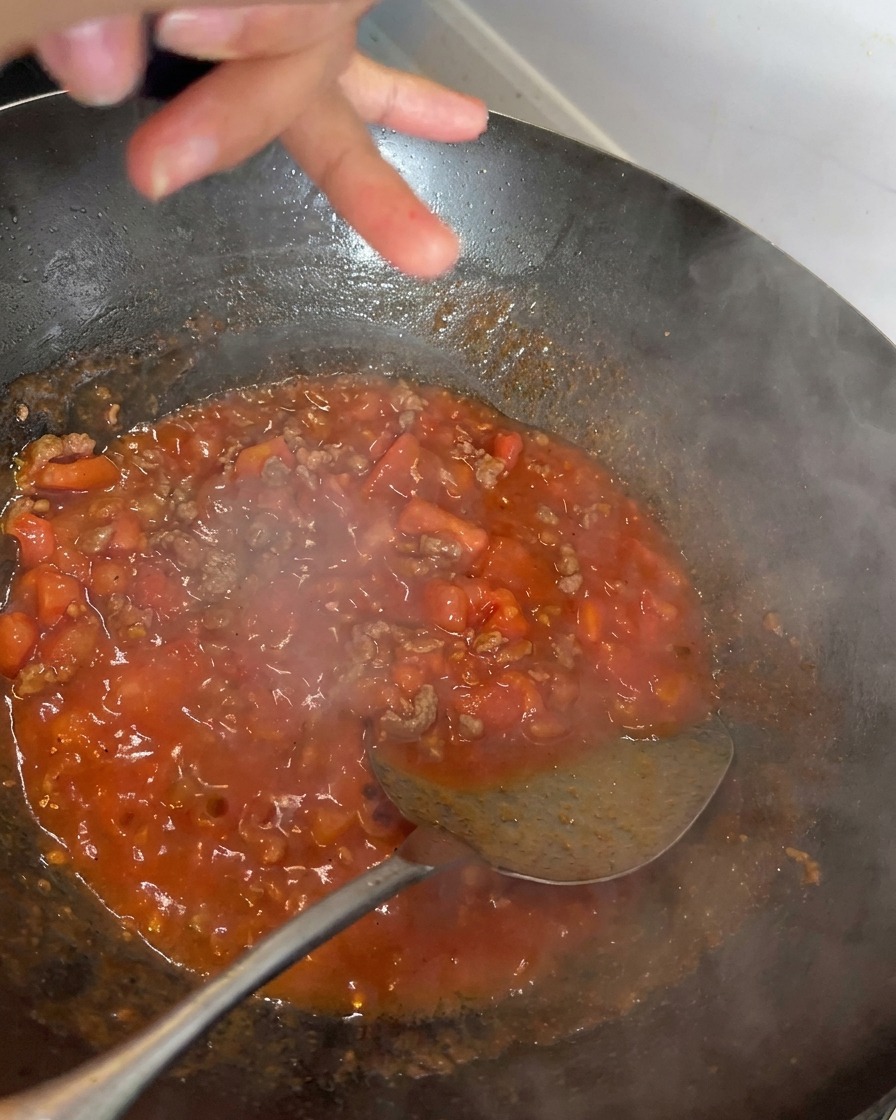 Pimienta negra recién molida cayendo sobre una salsa de tomate y ternera burbujeante en un wok.