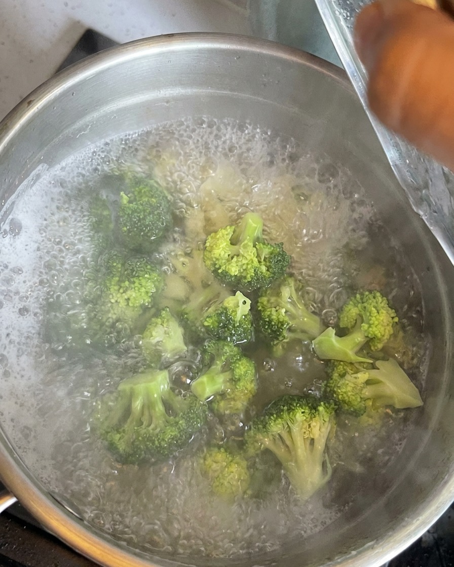 Floretes de brócoli verde brillante sumergidos en agua hirviendo con los macarrones.