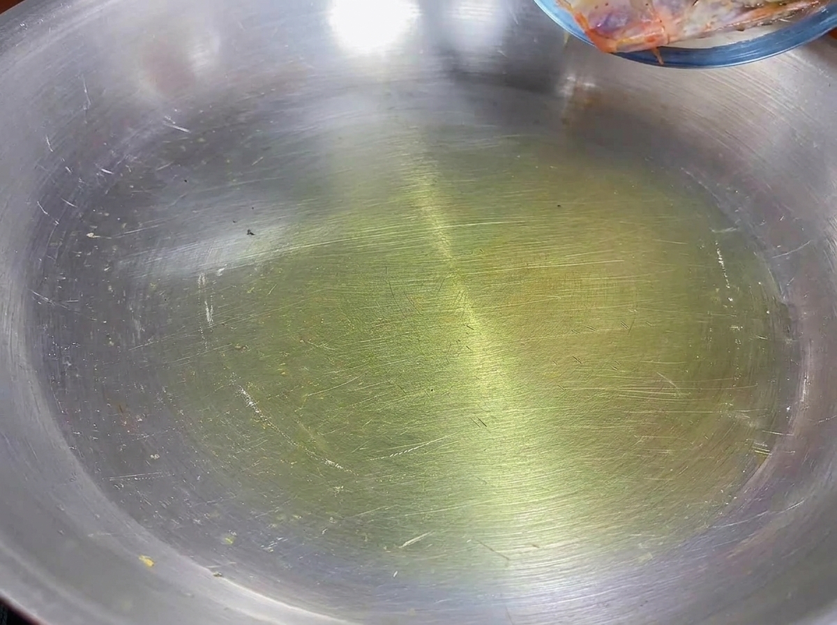 Cabezas de camarón friéndose en aceite de oliva en una sartén de acero inoxidable.