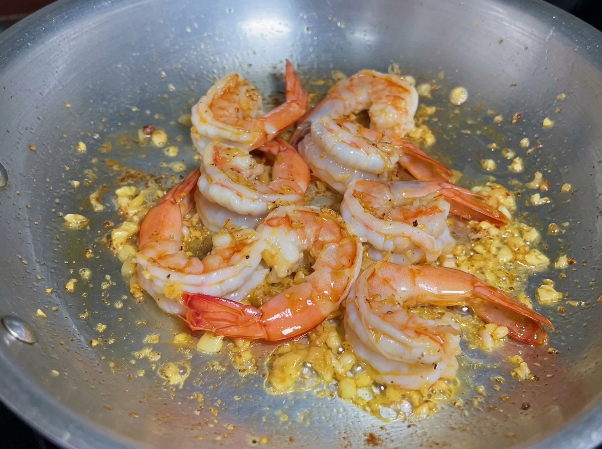 Líquido vertiéndose en una sartén con camarones cocidos para desglasar y recoger los sabores.