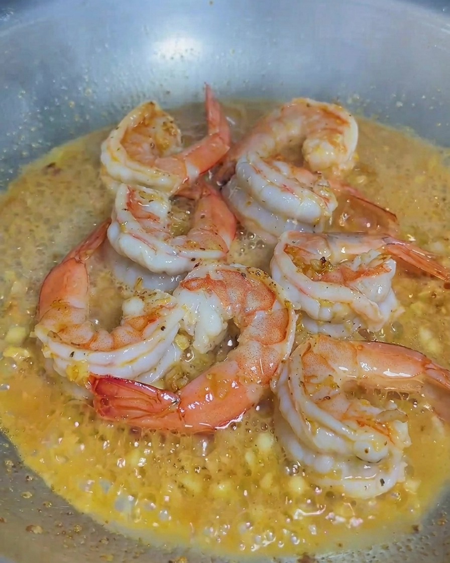 Crema de leche vertiéndose en una sartén que contiene camarones cocidos y ajo picado.