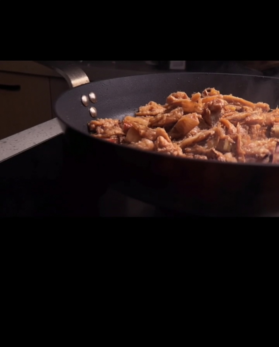 Espaguetis siendo mezclados con la salsa de carne en una sartén.