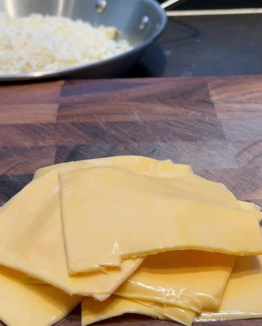 Lonchas de queso cheddar cortadas en trozos más pequeños sobre una tabla de madera.