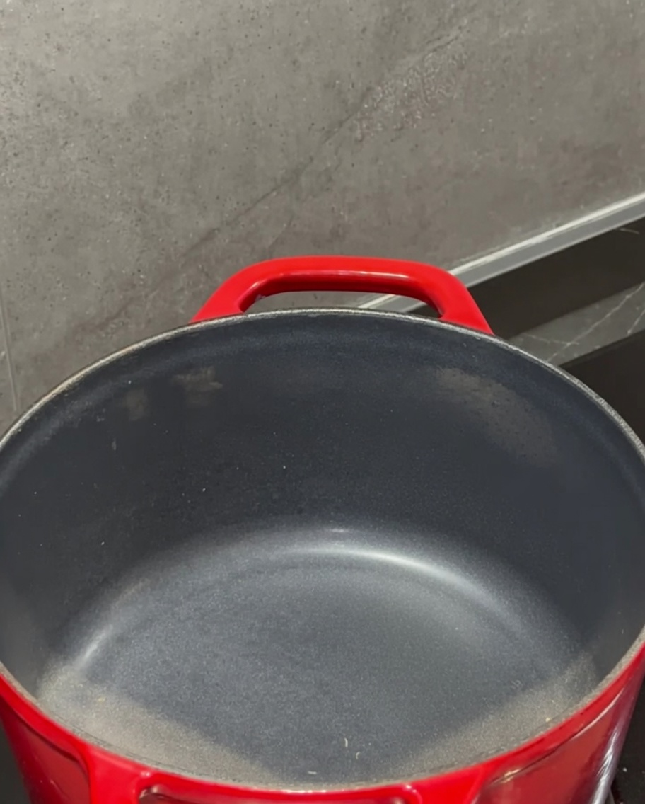 Un bloque de mantequilla derritiéndose en una olla roja sobre la estufa.