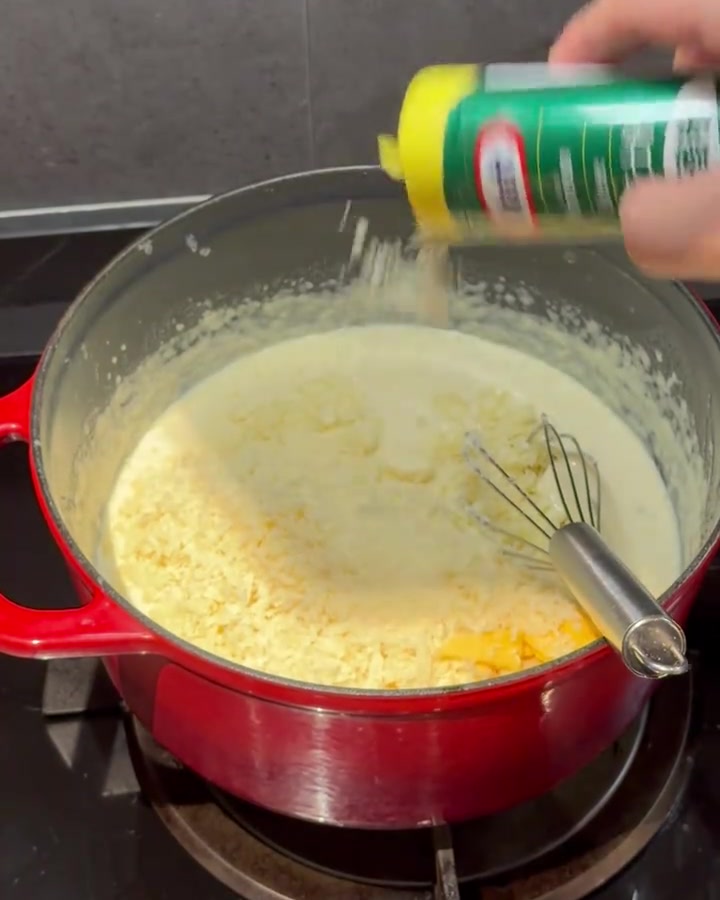Queso en polvo siendo batido en una salsa cremosa dentro de una olla roja.