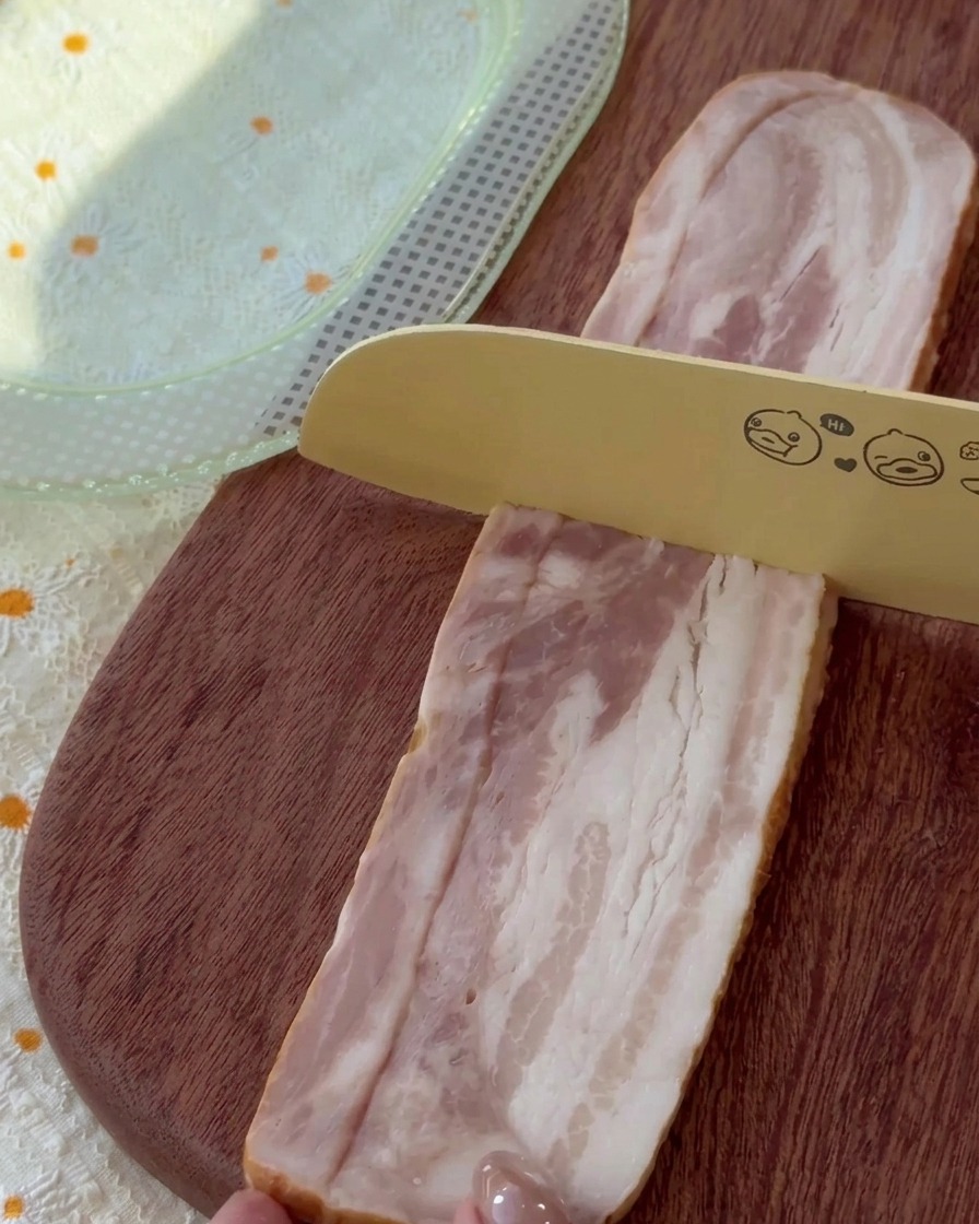 Tiras de bacon crudo cortadas en trozos uniformes sobre una tabla de madera.