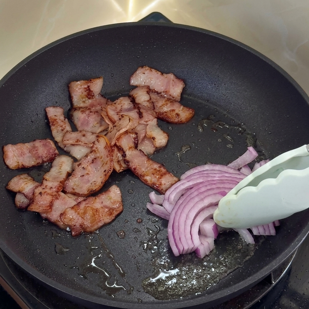 Cebolla morada cocinándose en la grasa del bacon junto al bacon crujiente.