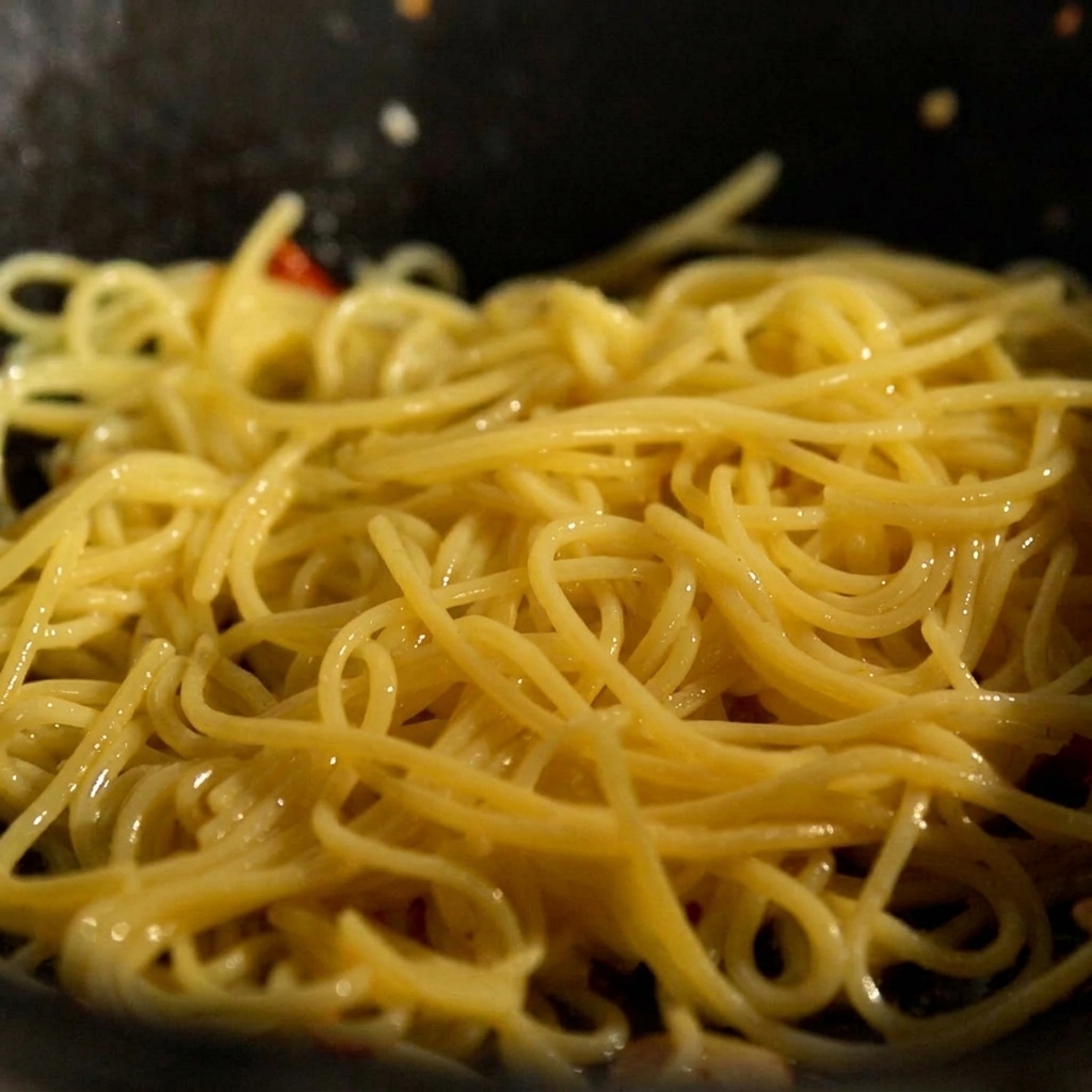 Fideos cocidos y un trozo de mantequilla añadiéndose a una sartén con ajo y chile salteados.