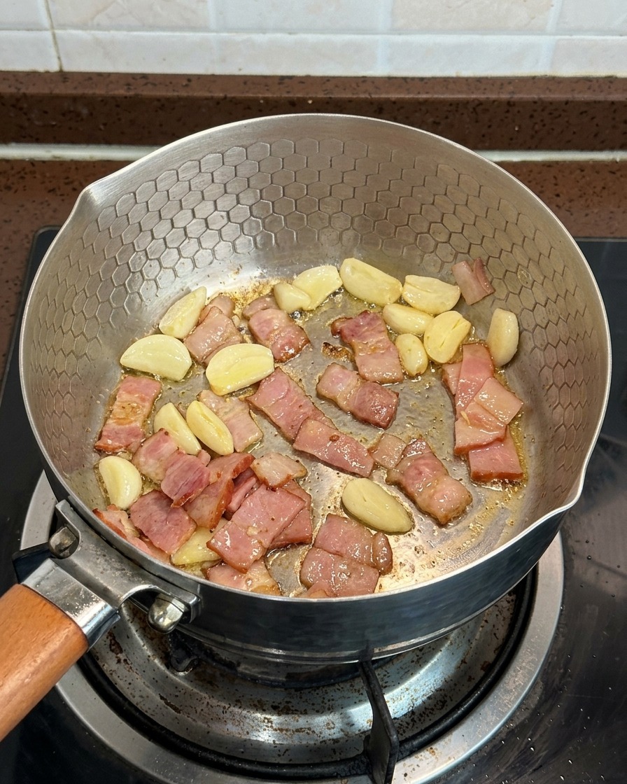 Champiñones laminados, trozos de beicon y láminas de ajo cocinándose juntos en una sartén.