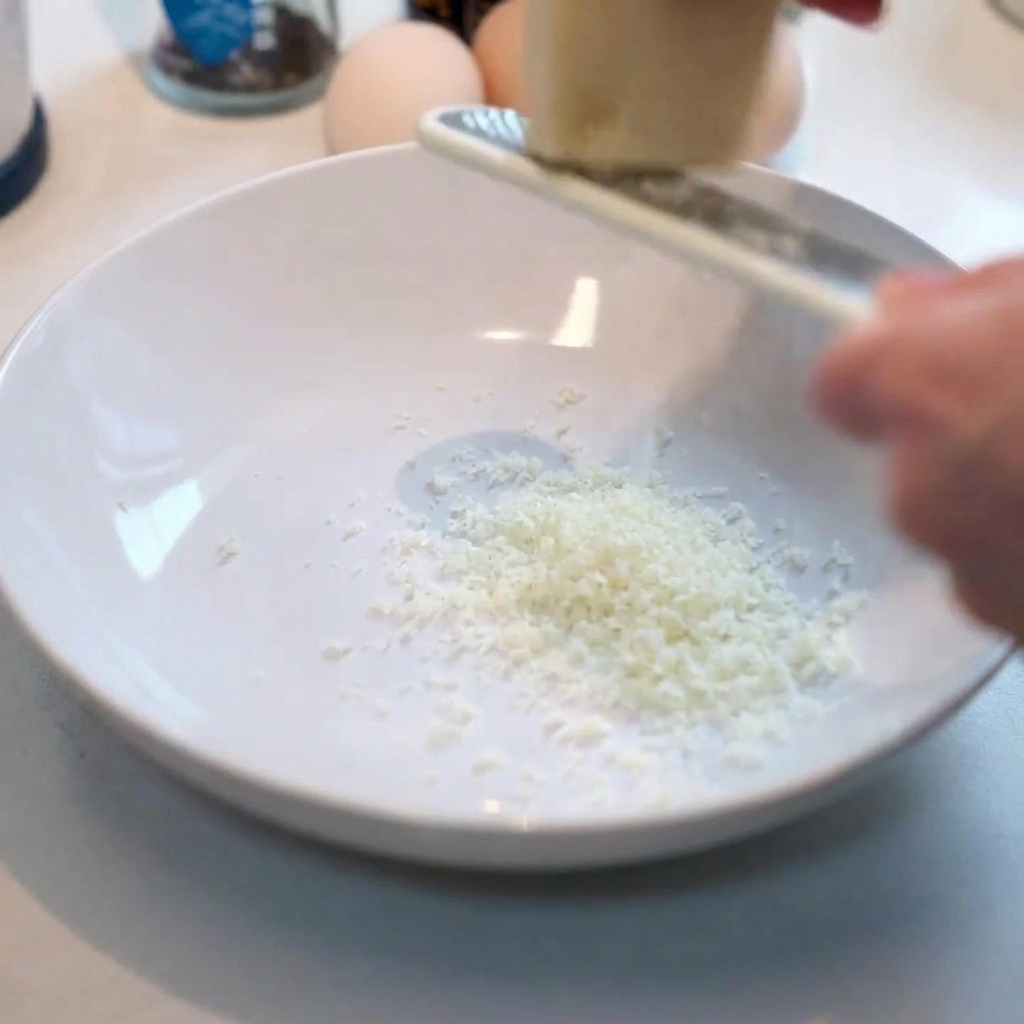 Rallando queso parmesano fresco en un bol blanco limpio.