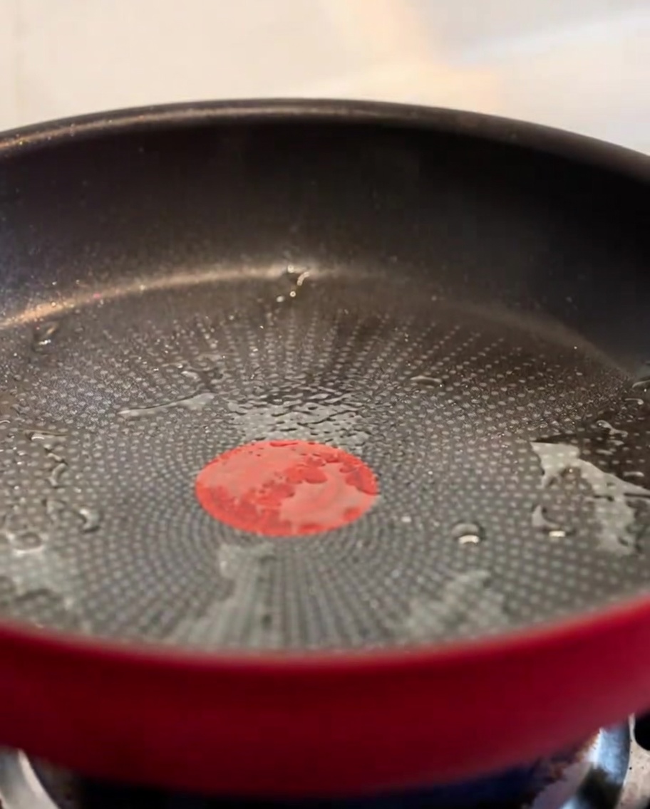 Trocitos de bacon crujiente chisporroteando en una sartén roja.