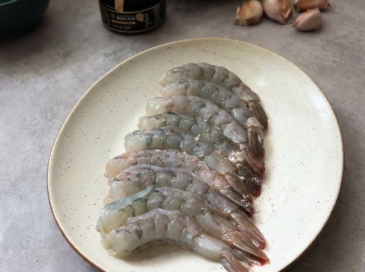 Gambas crudas peladas dispuestas en un plato, ligeramente sazonadas con sal y pimienta negra.