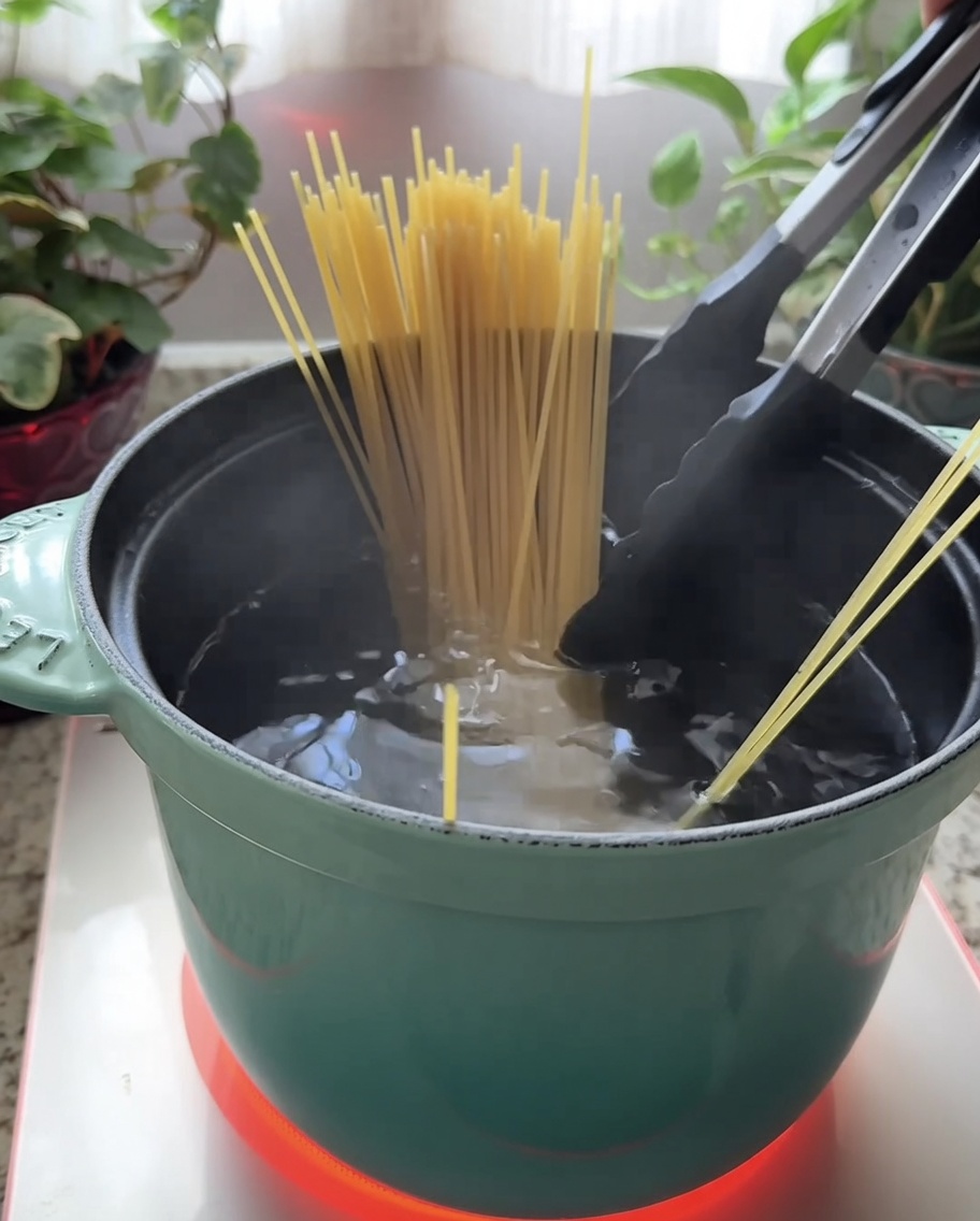 Espaguetis secos siendo sumergidos en una olla color turquesa llena de agua hirviendo.