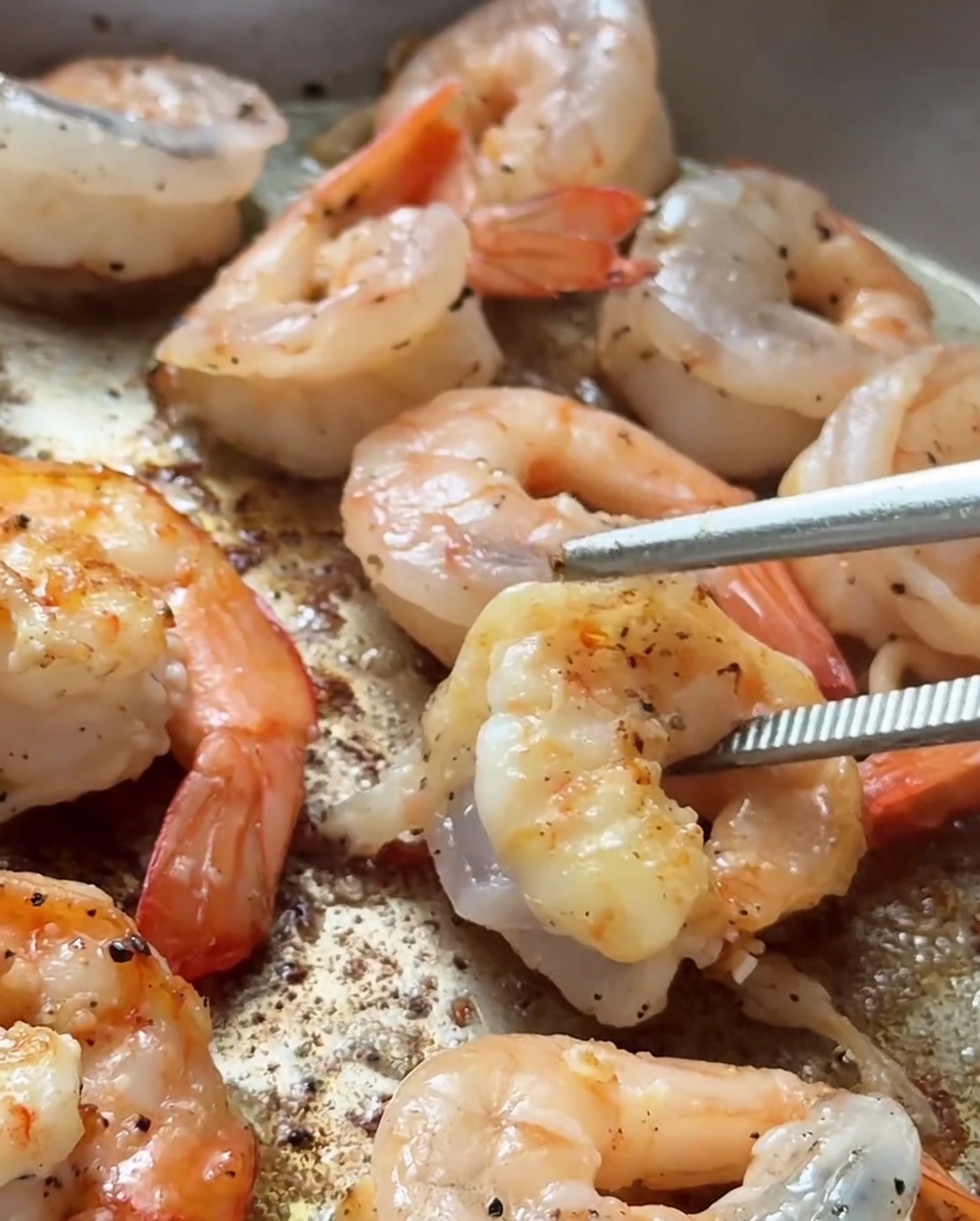 Gambas sellándose en una sartén caliente con un dorado visible en los bordes.