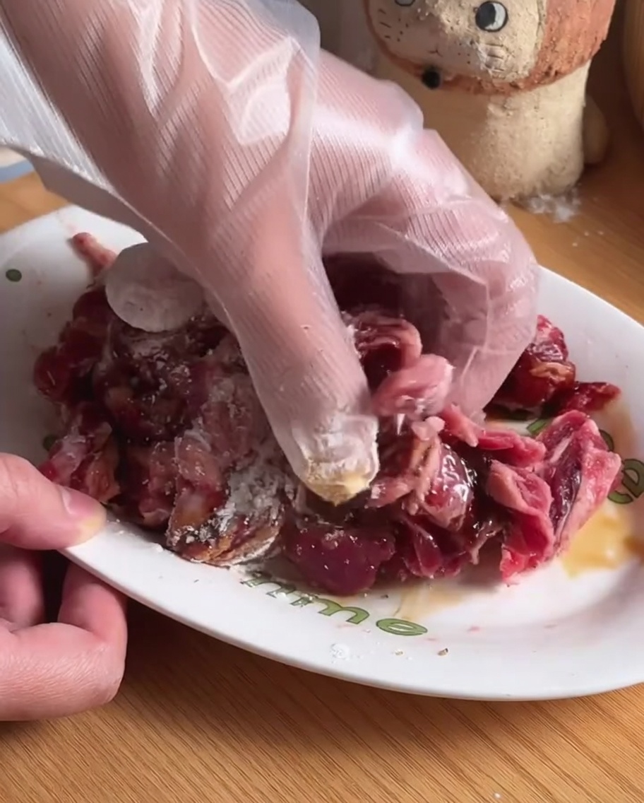 Tiras de ternera mezclándose con condimentos e ingredientes de marinado en un cuenco blanco.