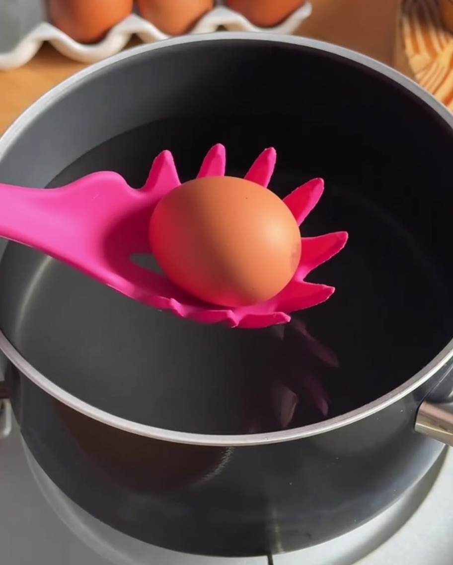 Un huevo siendo introducido en una olla de agua caliente con una cuchara de silicona ranurada.