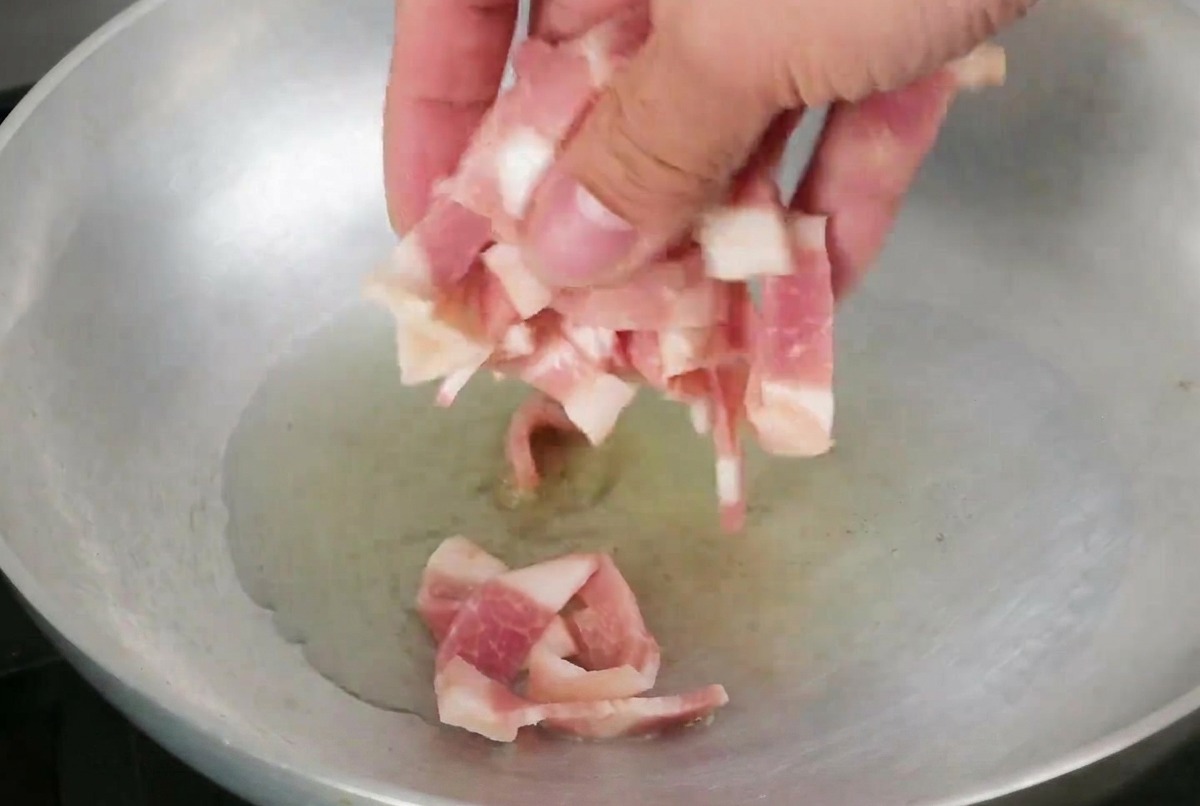 Tiras de tocino friéndose en una sartén con aceite de oliva brillante.