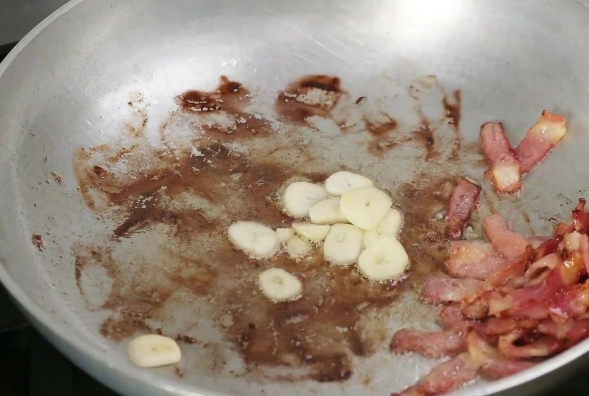 Ajo y champiñones en rodajas dorándose en una sartén junto al tocino crujiente.