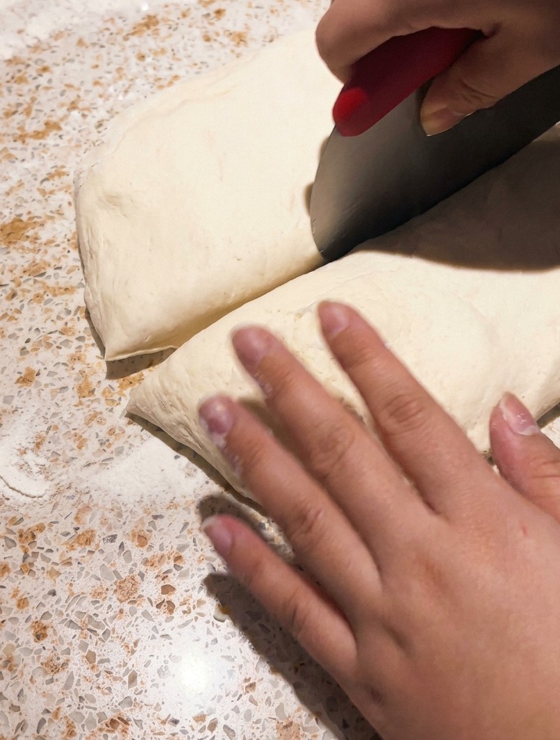 Una rasqueta de metal cortando un trozo de masa de pizza fermentada sobre una encimera.