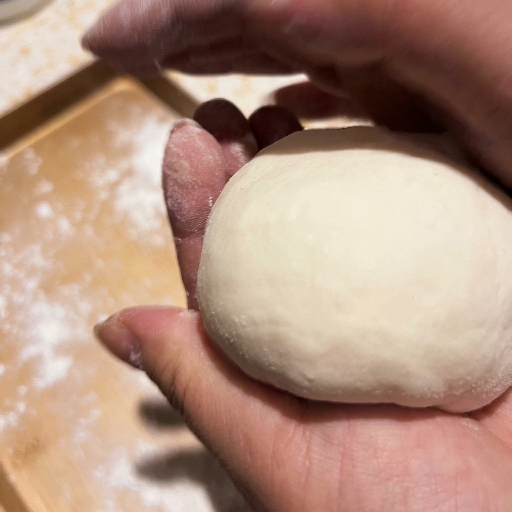 Manos ahuecando y dando forma de bola suave a un trozo de masa de pizza cruda.