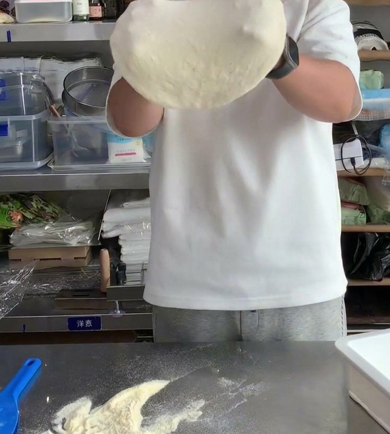 Masa de pizza siendo estirada sobre los nudillos para aumentar su diámetro y adelgazar el centro.