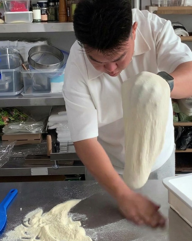 Manos moviendo la masa de pizza estirada de un lado a otro para sacudir el exceso de harina.