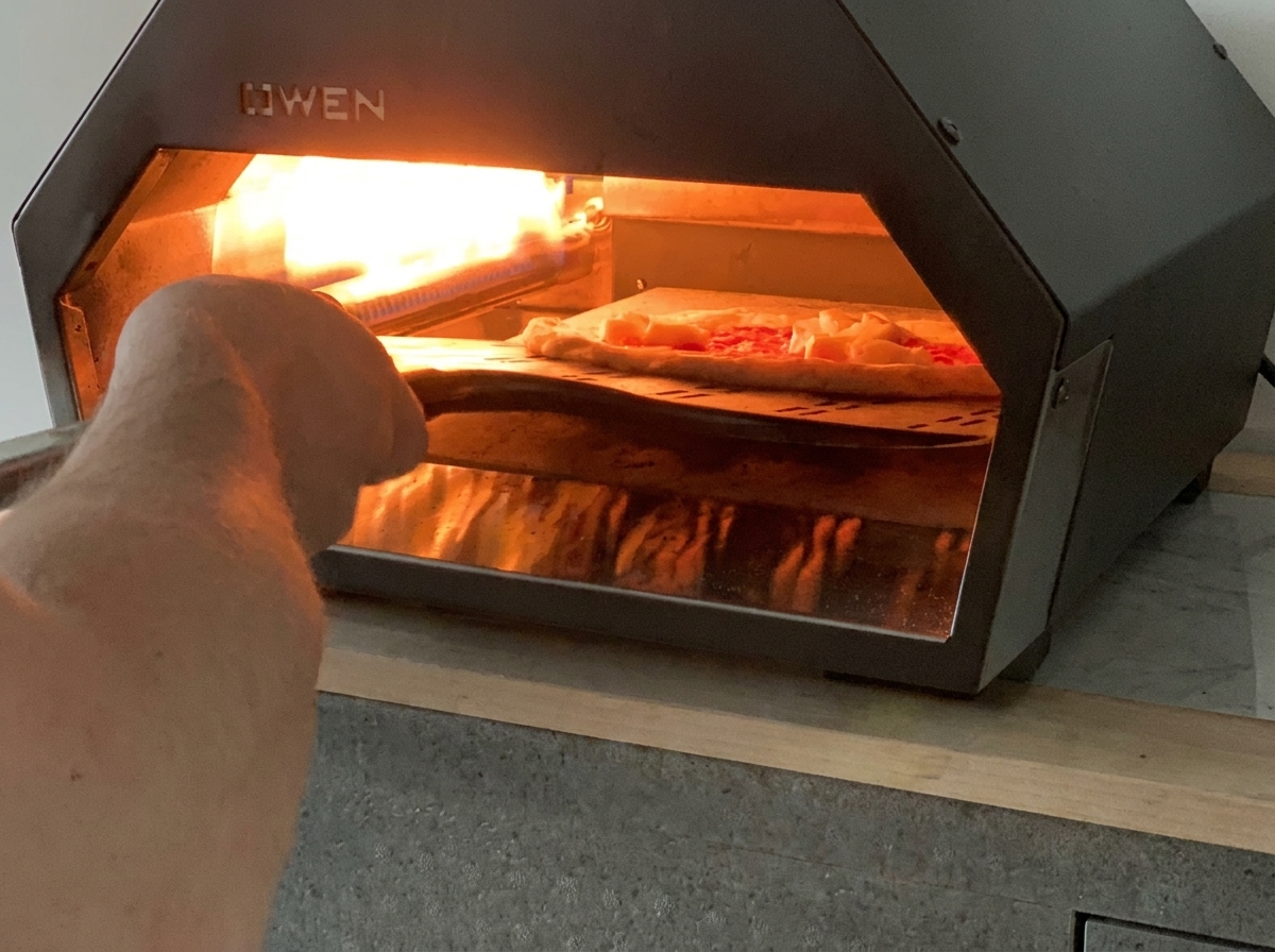 Una pala de pizza deslizando una pizza Margarita sin hornear en un horno de gas de mesa caliente.