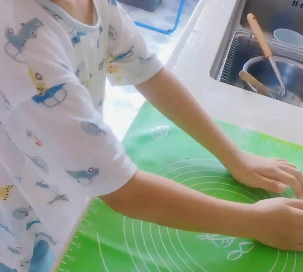 Una bola de masa de pizza siendo amasada sobre una esterilla de silicona verde.