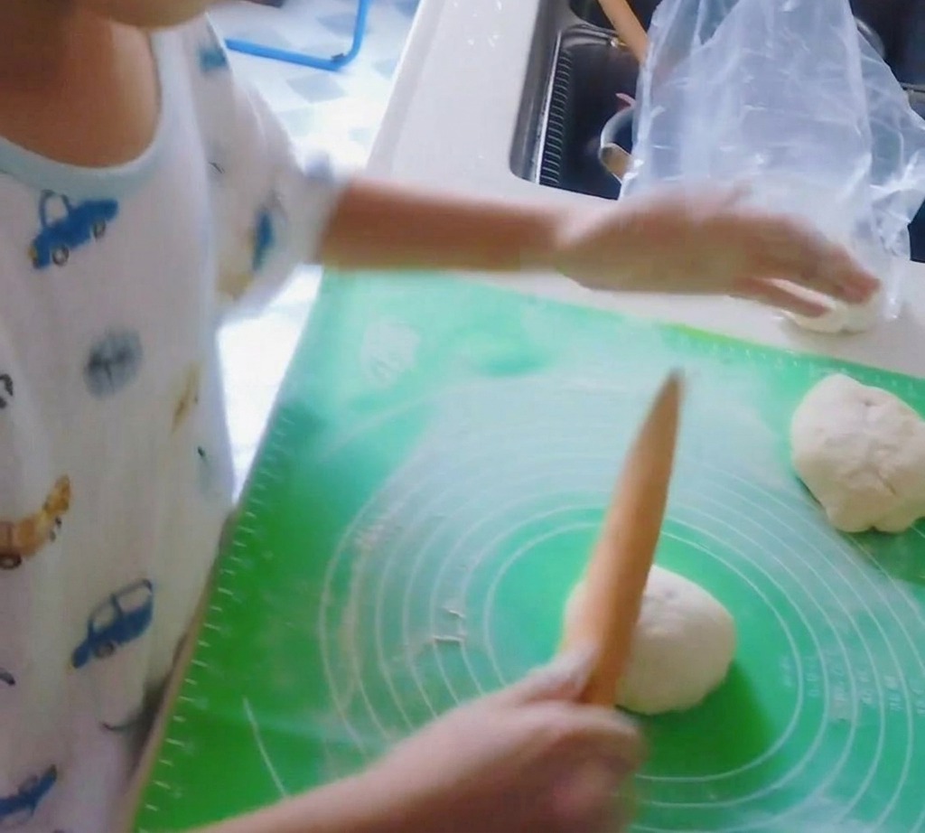 Un rodillo de madera aplanando una bola de masa de pizza para formar una base circular.