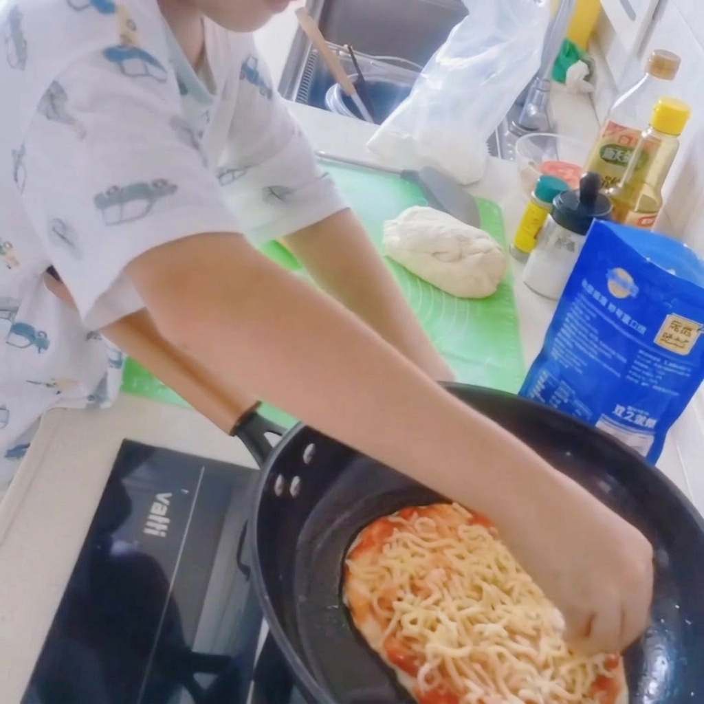 Primer plano de una base de pizza en una sartén siendo cubierta con una capa de queso mozzarella rallado.