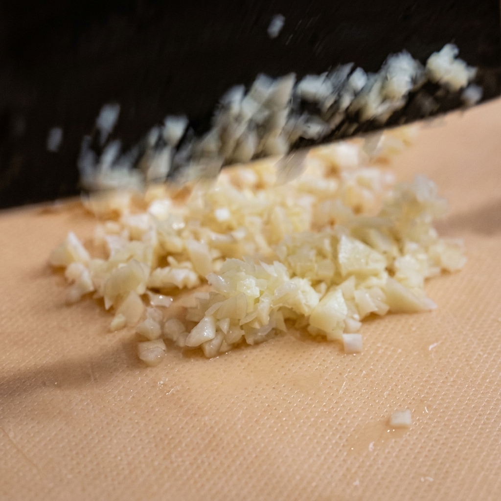 Trozos de ajo finamente picados esparcidos sobre una tabla de cortar de color claro.