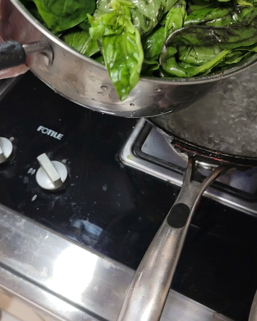 Hojas de albahaca fresca sumergidas en una olla con agua hirviendo al fuego.