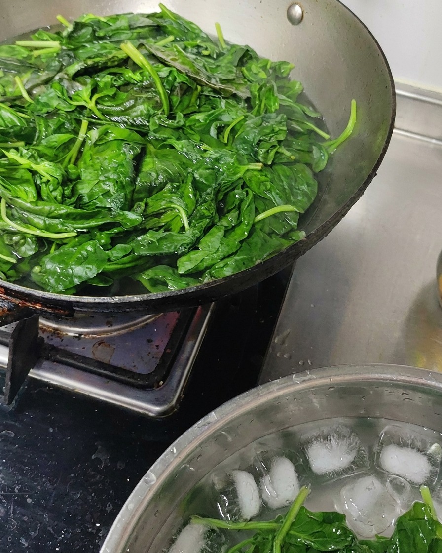 Hojas de albahaca recién blanqueadas enfriándose en un bol con agua y hielo.