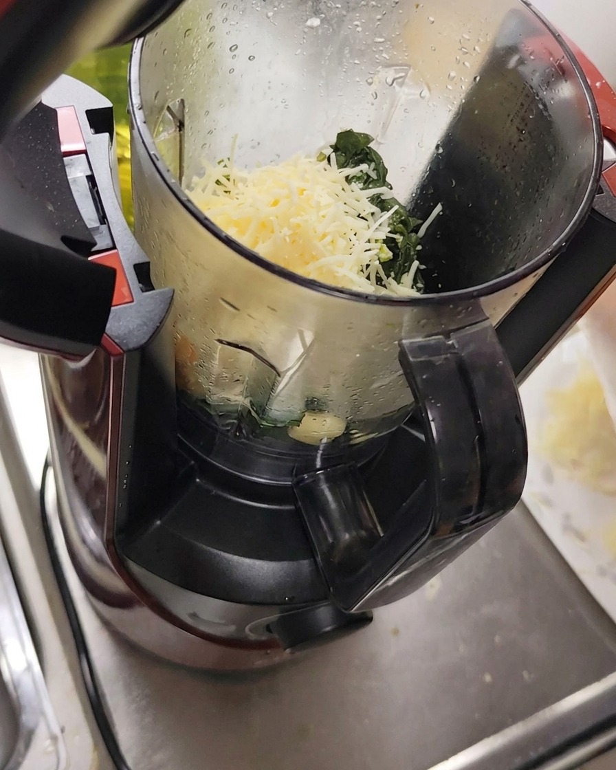 Queso rallado, ajo y piñones en un procesador de alimentos junto a las hojas de albahaca.
