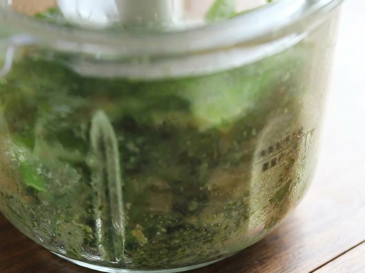 Vista en primer plano del bol del procesador de alimentos que muestra el pesto de albahaca recién triturado de color verde brillante.