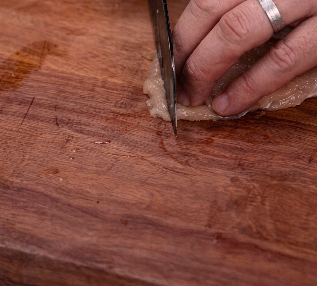 Pechuga de pollo cruda siendo cortada en tiras uniformes sobre una tabla de madera.
