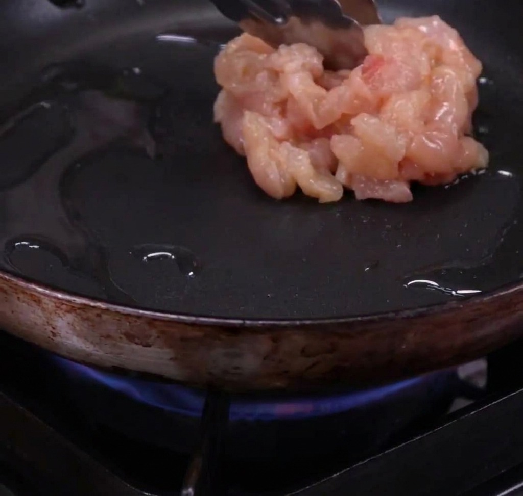 Tiras de pollo dorándose en una sartén caliente con aceite de oliva.