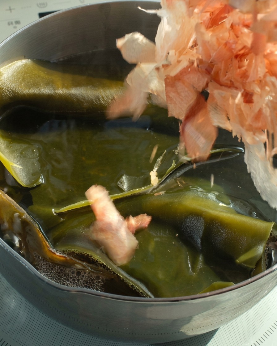 Copos de bonito cayendo en una olla de caldo de kombu caliente.